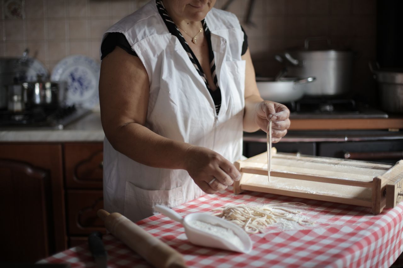 An elderly woman skillfully prepares homemade pasta on a kitchen counter, showcasing traditional cooking techniques.