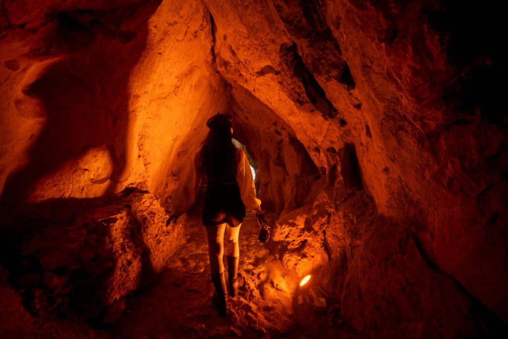 A woman explores a dimly lit cave, revealing rocky textures and shadows in warm light.