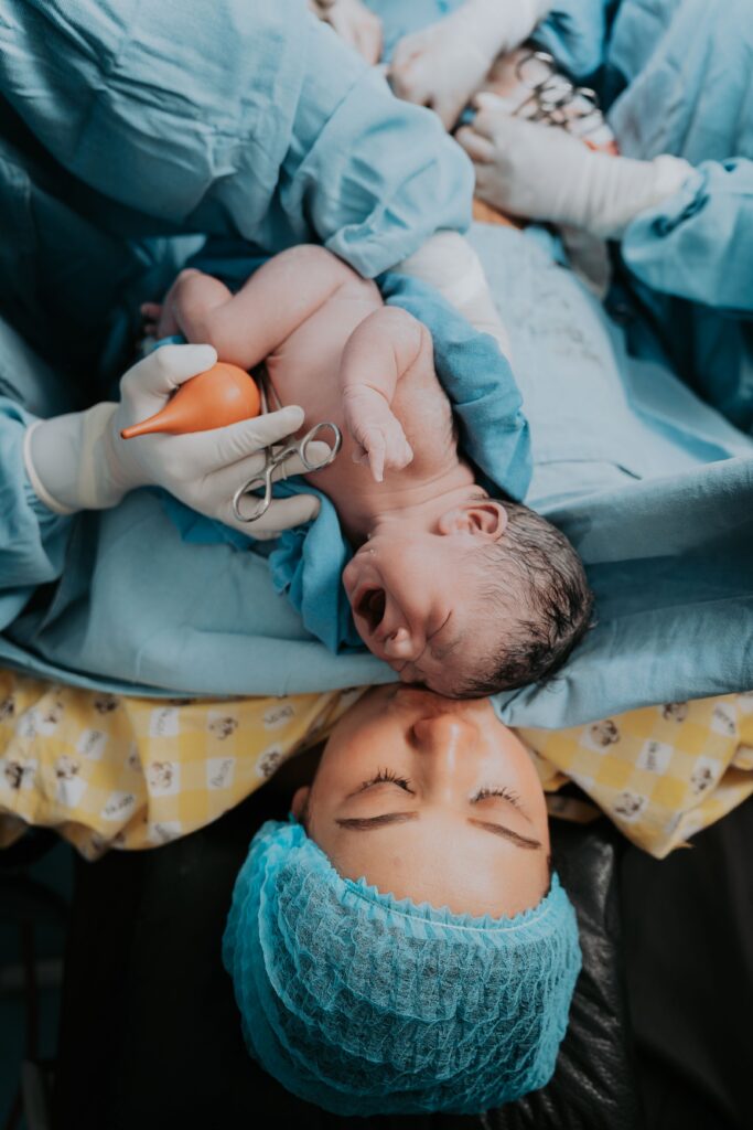 Newborn baby held by medical staff beside mother post-delivery in Mexican hospital.