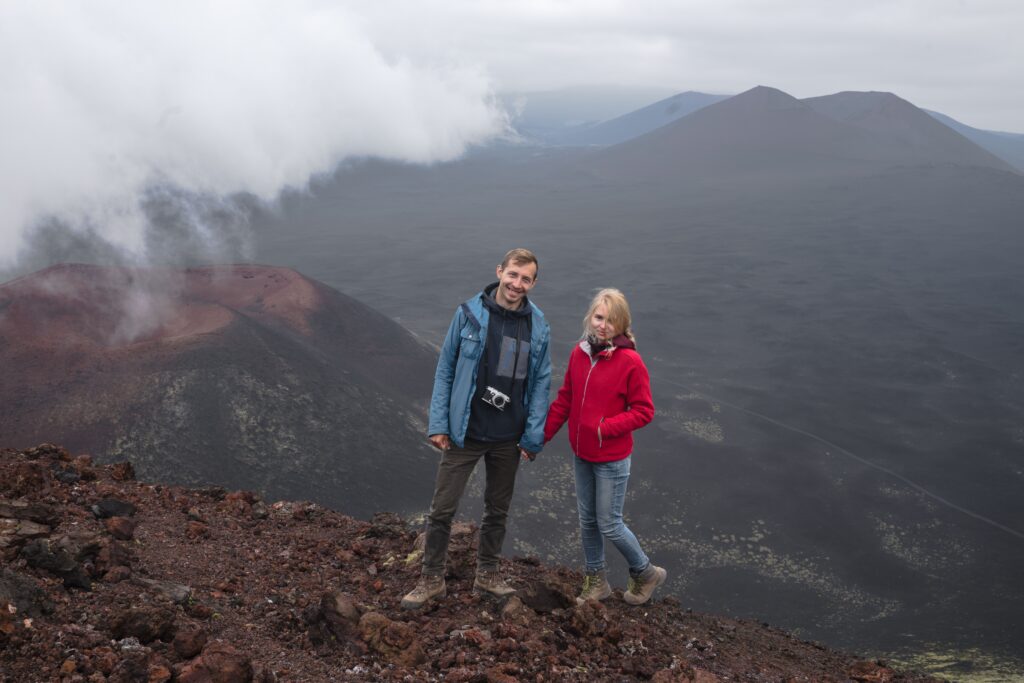 A couple explores the summit of a volcanic mountain, capturing the dramatic landscape.