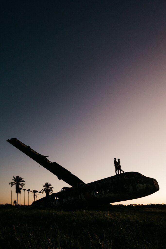 From below side view of anonymous couple silhouettes embracing on abandoned airplane after accident under sky at dusk