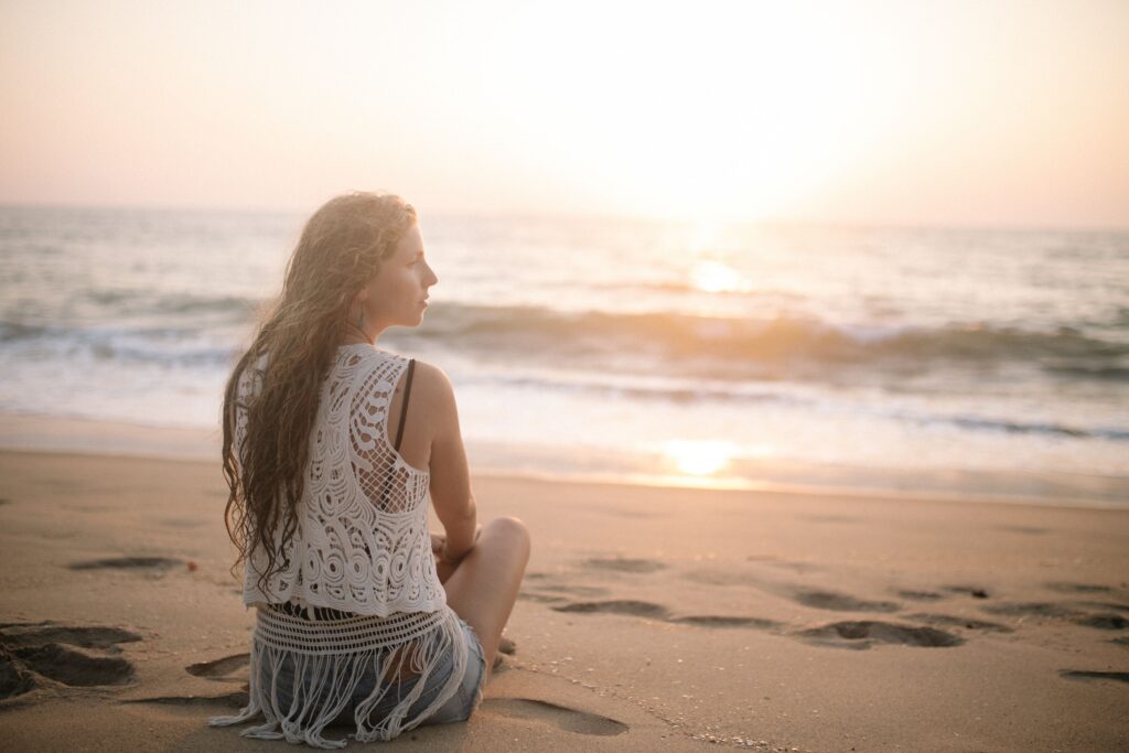 A woman enjoys peaceful meditation on a sandy beach during sunrise, embracing solitude and tranquility.