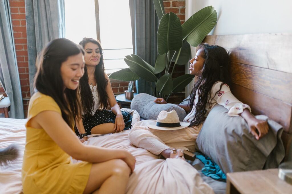 Three diverse women enjoying a relaxed conversation in a cozy bedroom setting, embodying friendship and comfort.