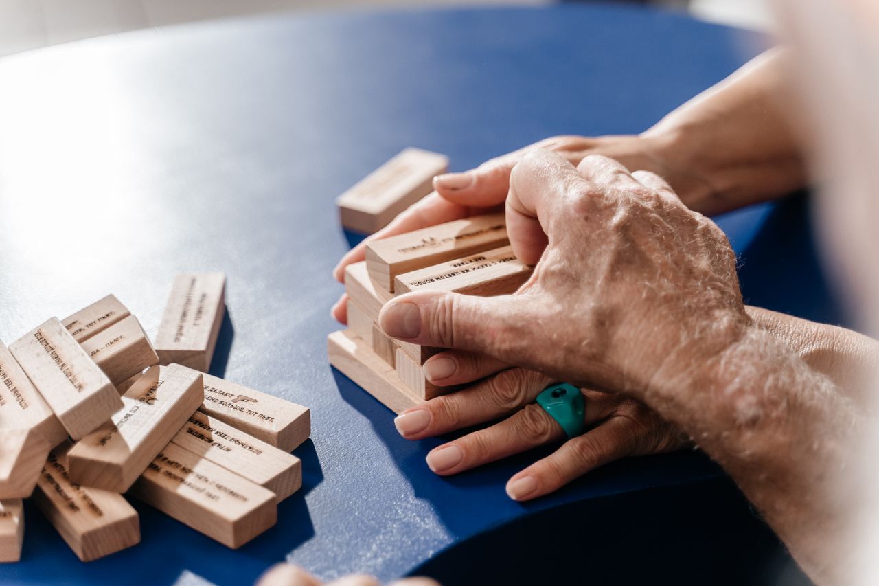 Close-up of hands stacking wooden blocks on a blue table, emphasizing teamwork and interaction.