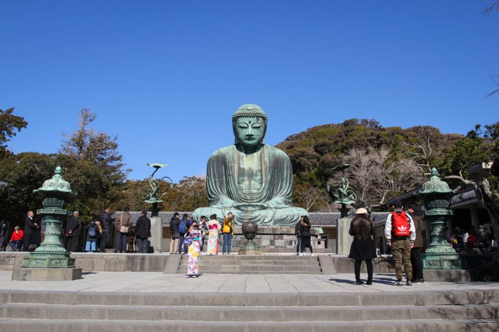 Great Buddha statue in Kamakura, Japan surrounded by tourists on a clear day.