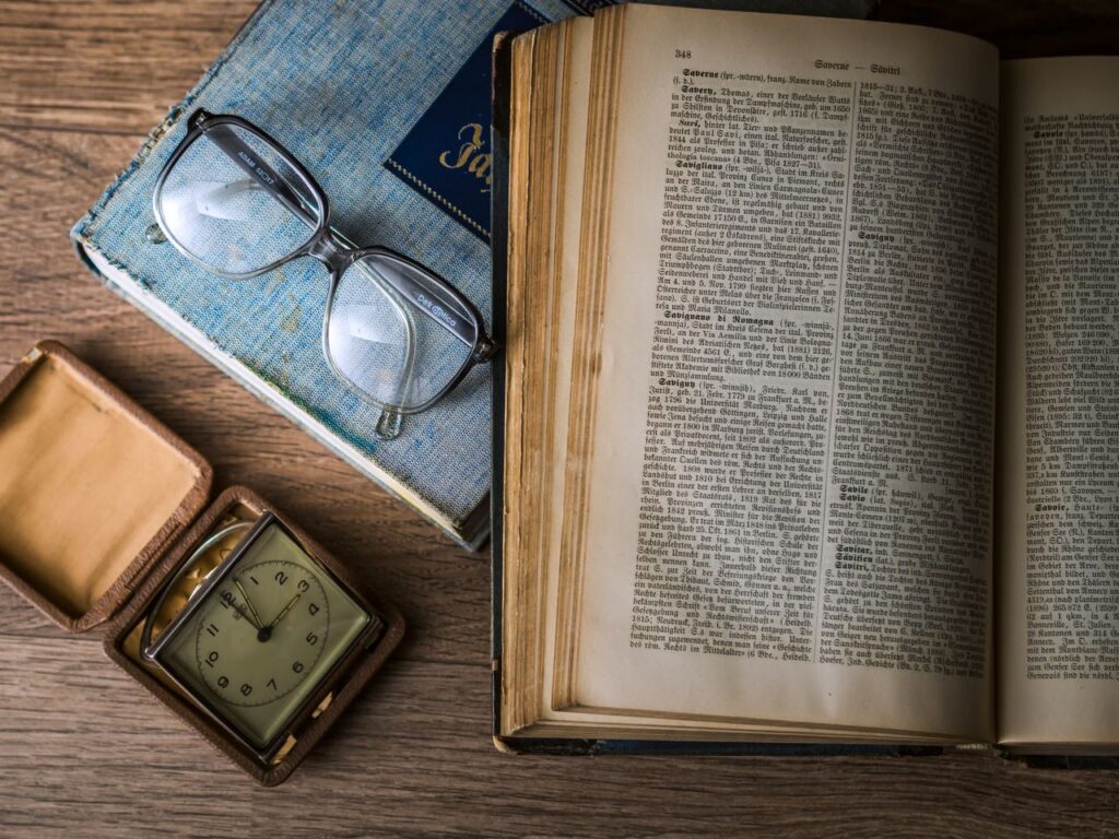 A vintage setting with antique books, watch, and reading glasses on a wooden table.