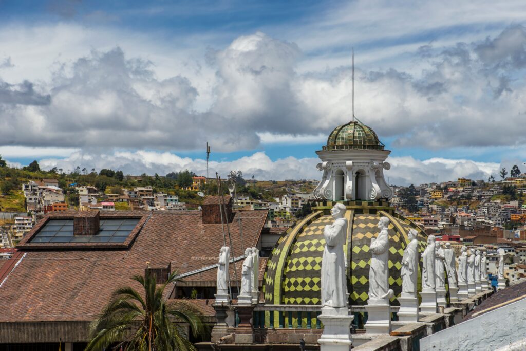 A beautiful architectural dome with statues viewed against an urban backdrop under a vibrant sky.