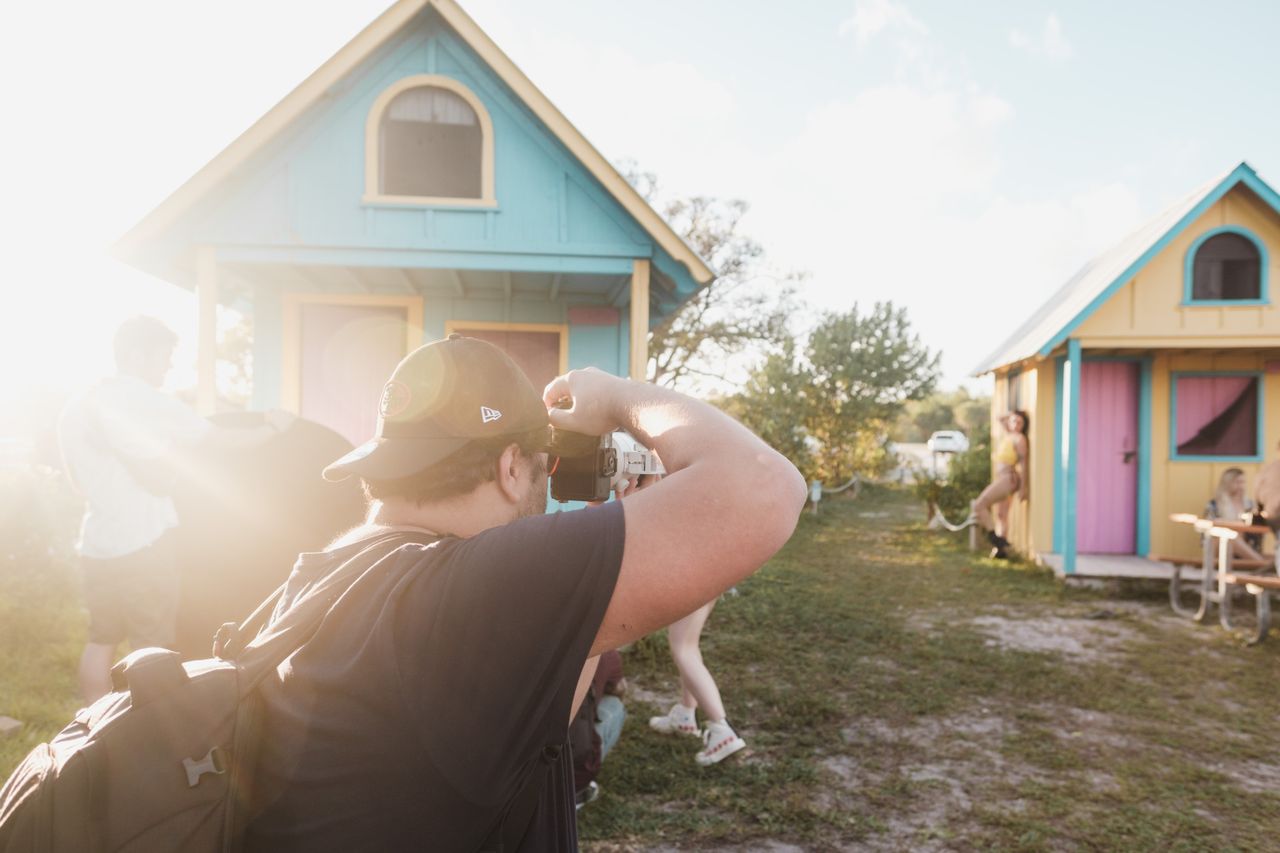 Photographer on a Miami beach capturing models near colorful huts in sunlight.
