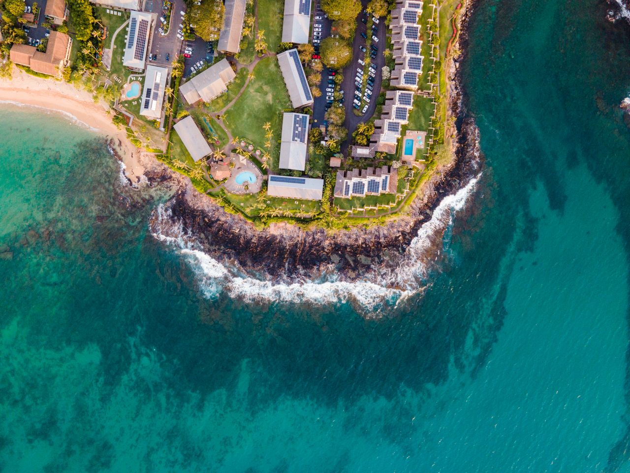 Stunning aerial shot of Lahaina, HI coastline with clear turquoise water and lush greenery.
