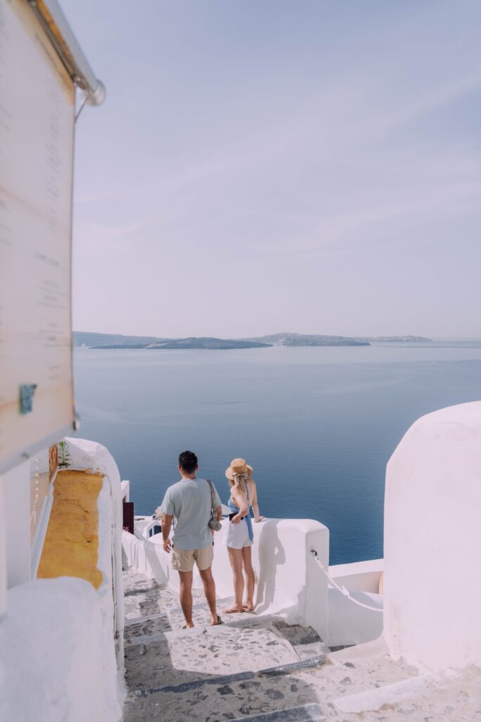 Two people walking down a stone staircase overlooking the sea in Santorini, Greece.