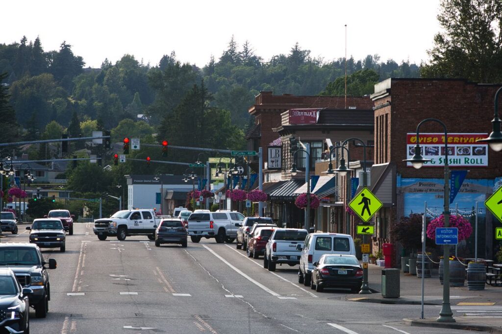 Lively urban street with cars, shops, and pedestrians during daytime.