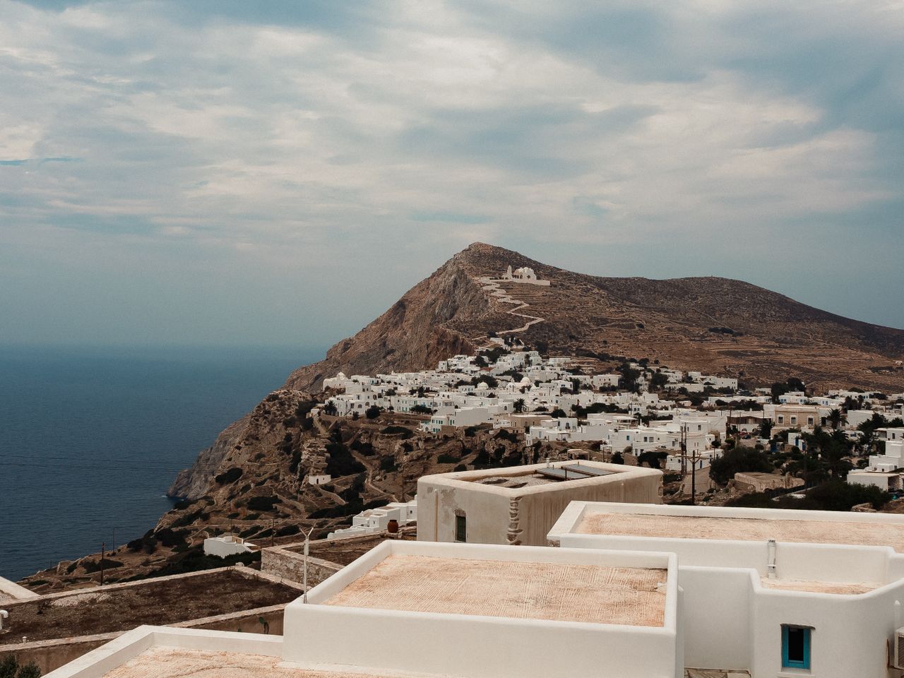 Capture of a beautiful white village atop a rugged cliff in Folegandros, Greece with the sea in the background.