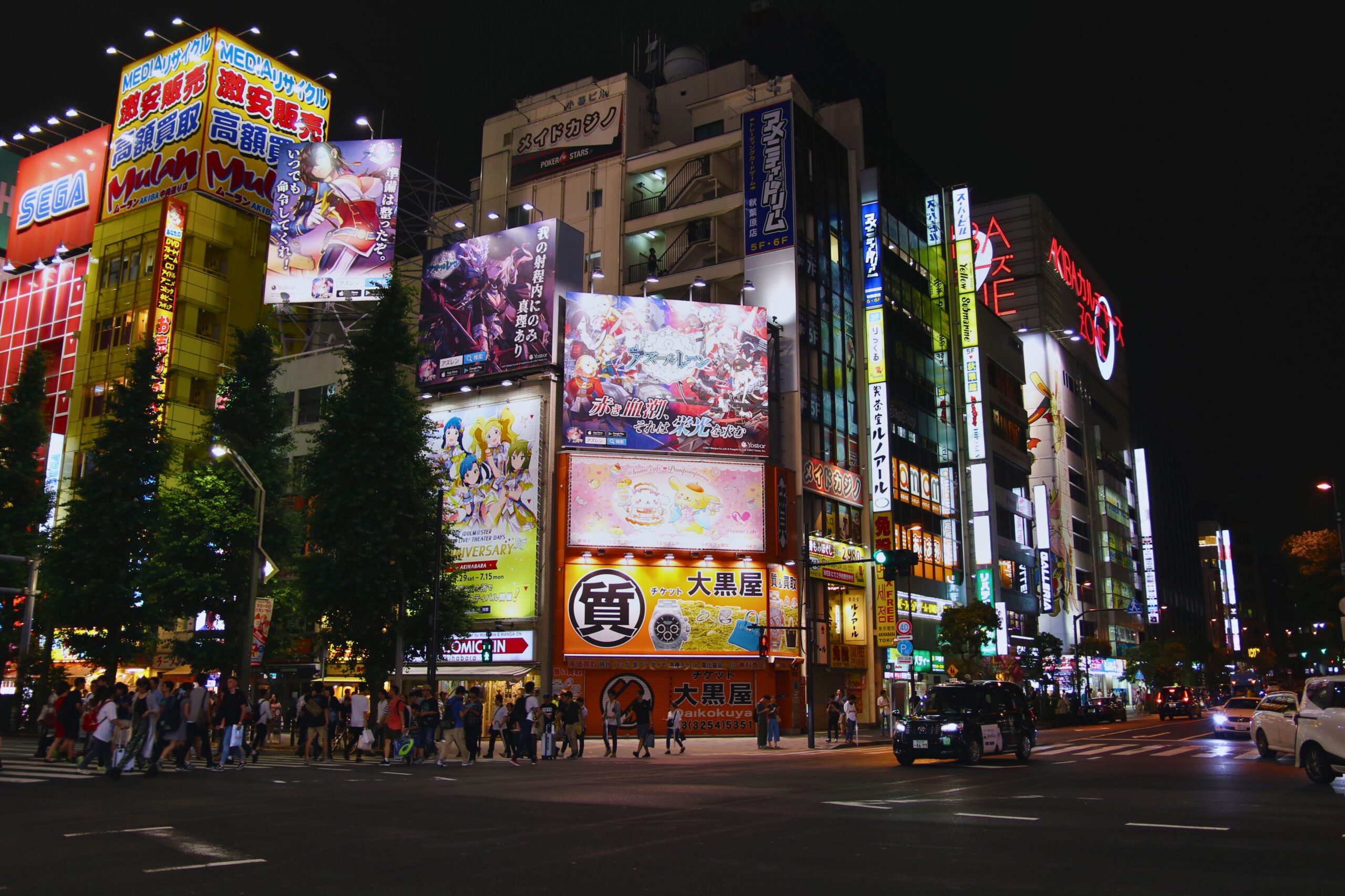 Bustling street scene in Akihabara, Tokyo at night with bright neon signs and animated billboards.