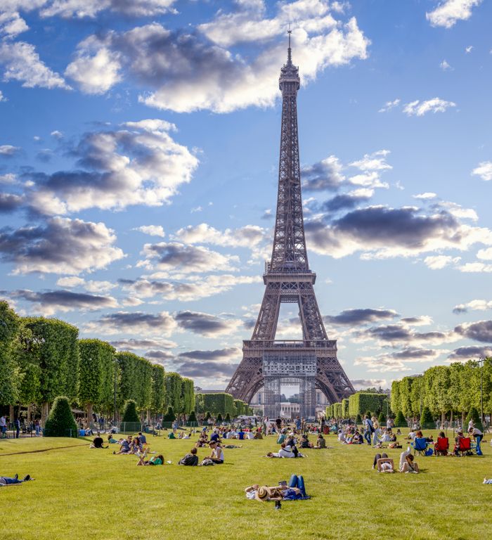A vibrant scene of people relaxing near the Eiffel Tower in Paris under a bright sky.