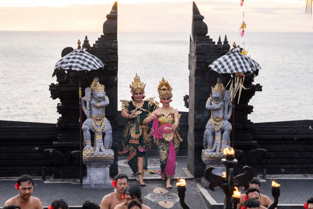 Balinese dancers perform at the iconic Uluwatu Temple during sunset, showcasing vibrant traditional attire.