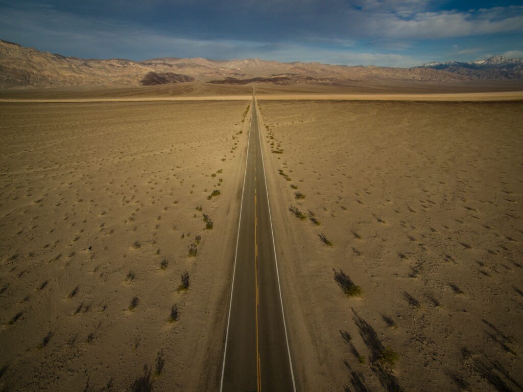 Aerial view of a long straight road cutting through the vast desert landscape in Death Valley.