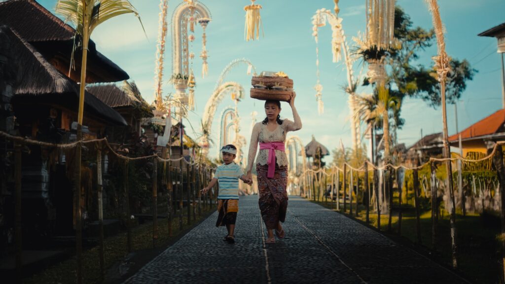 A Balinese mother and child walking in a decorated village street, showcasing cultural beauty.