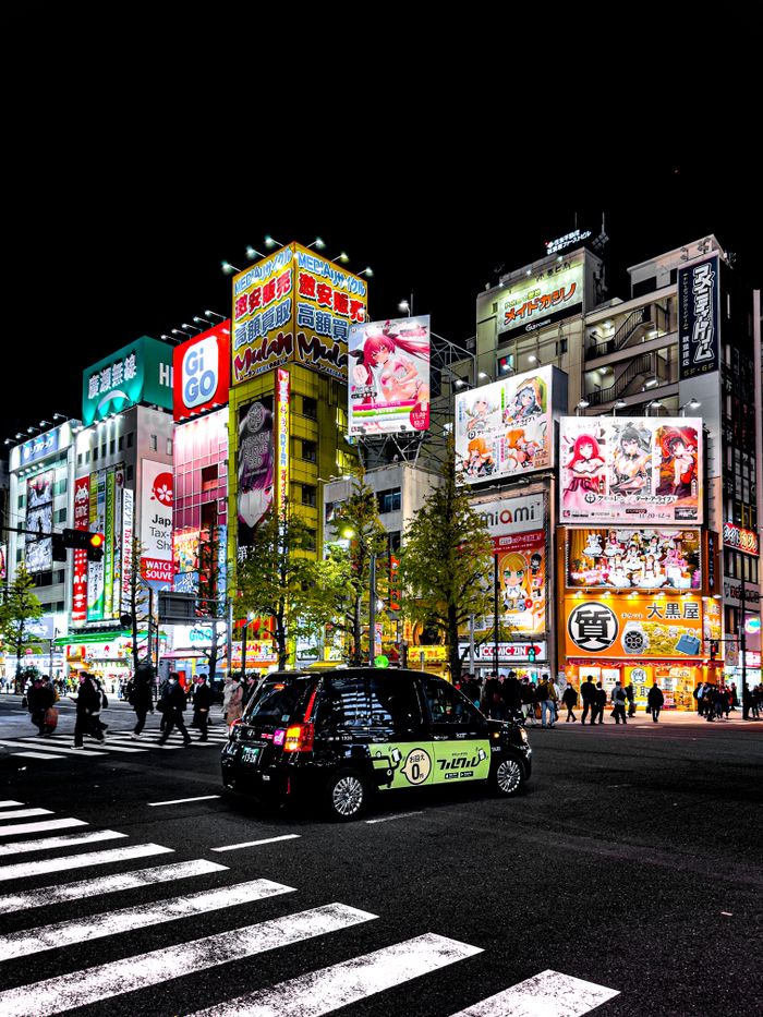 Bustling night scene in Akihabara, Tokyo with neon lights, billboards, and street life.