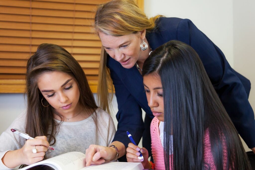 A teacher providing guidance to two students studying in a classroom. Ideal for educational content.