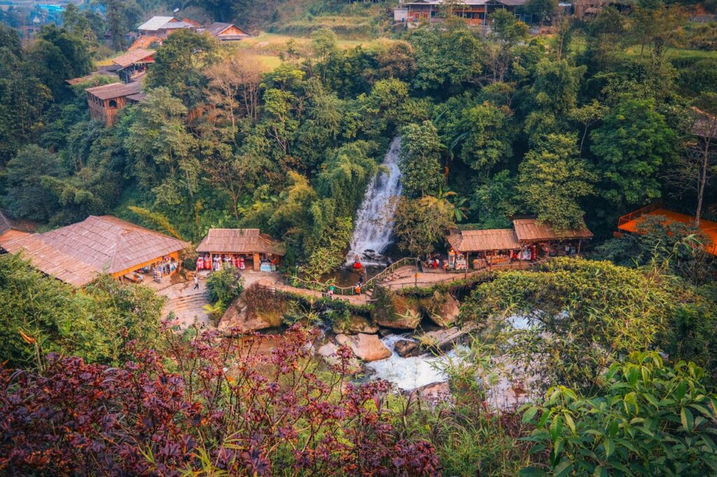 Aerial view of waterfall and houses surrounded by lush greenery in Sa Pa, Vietnam.
