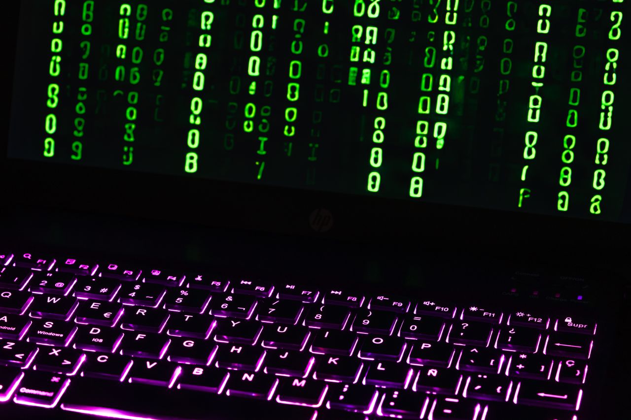 Illuminated laptop keyboard with Matrix-style green code cascading down screen.