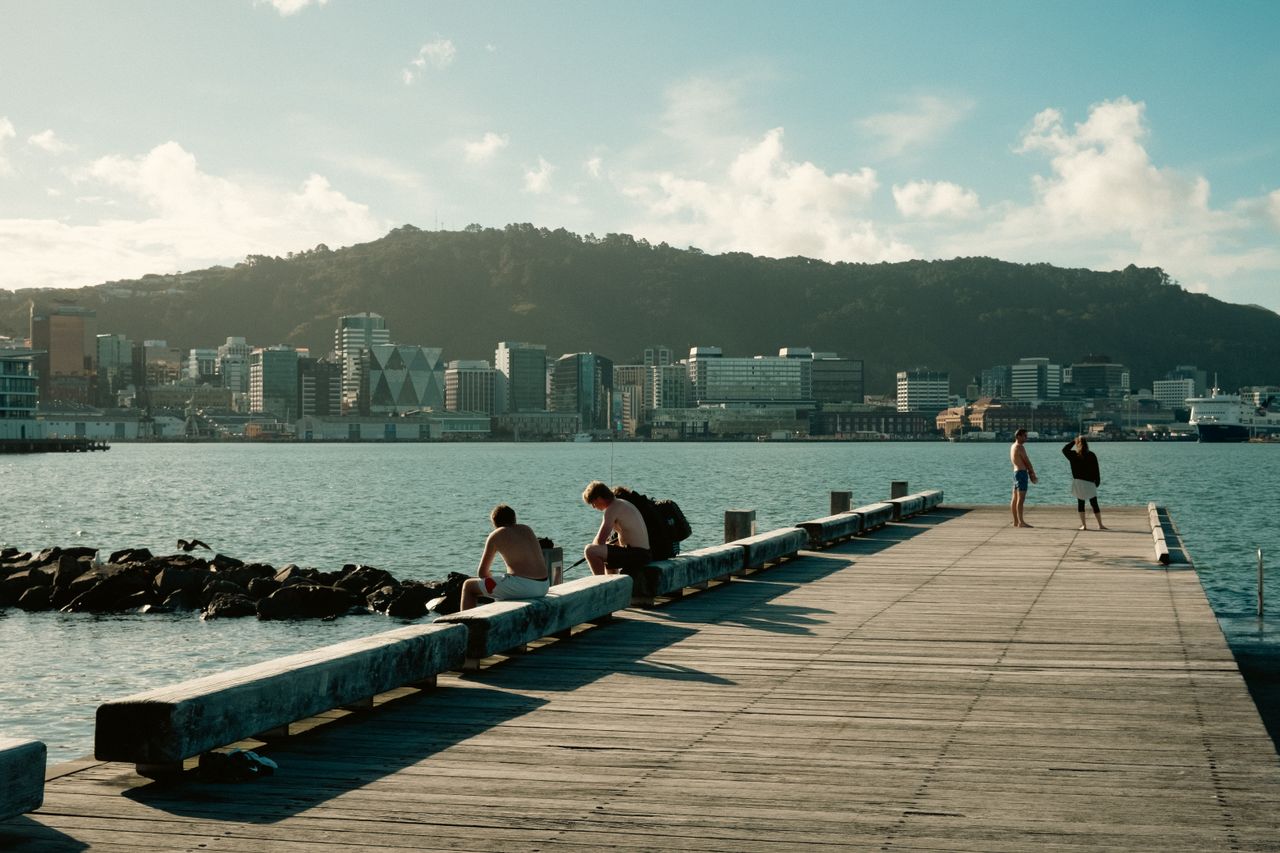 People enjoying a sunny day on the waterfront pier in Wellington, New Zealand with city skyline view.