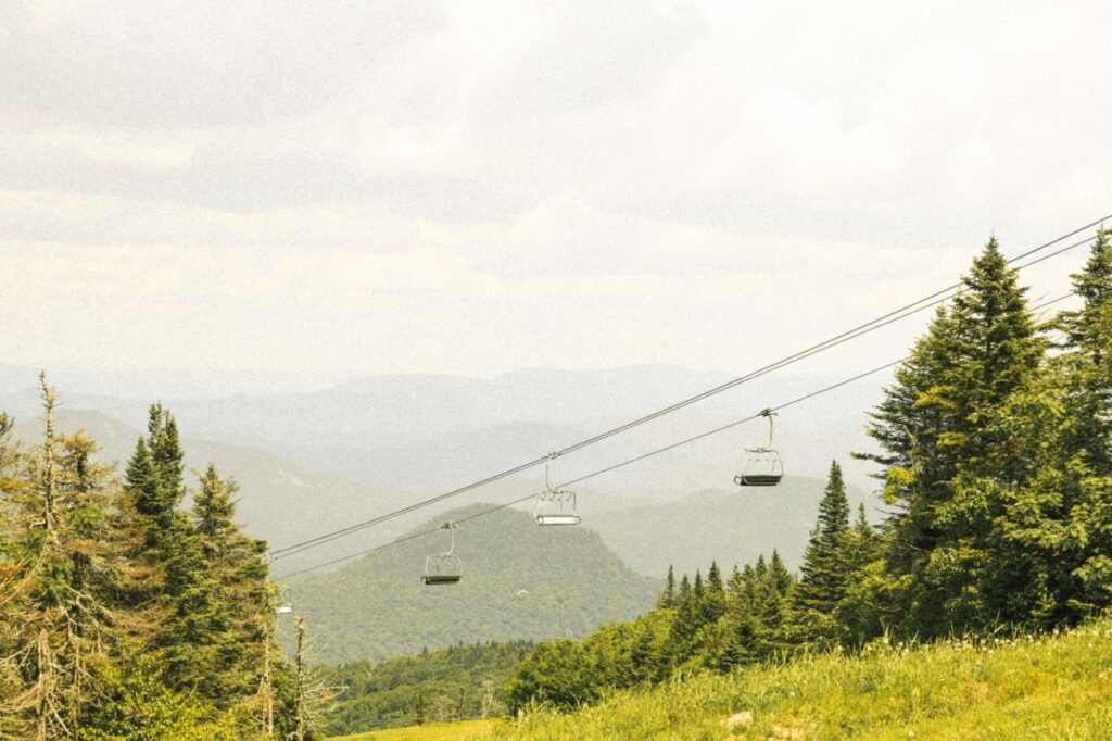Empty chairlifts on a mountain amidst summer greenery and distant hills.