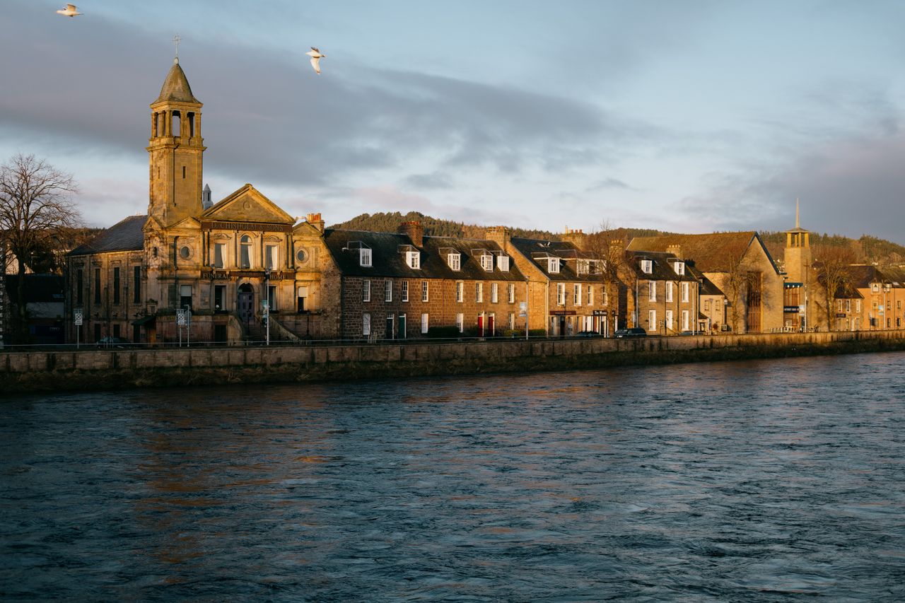 Scenic view of Inverness riverfront and historic buildings at sunrise with a serene river and seagulls.