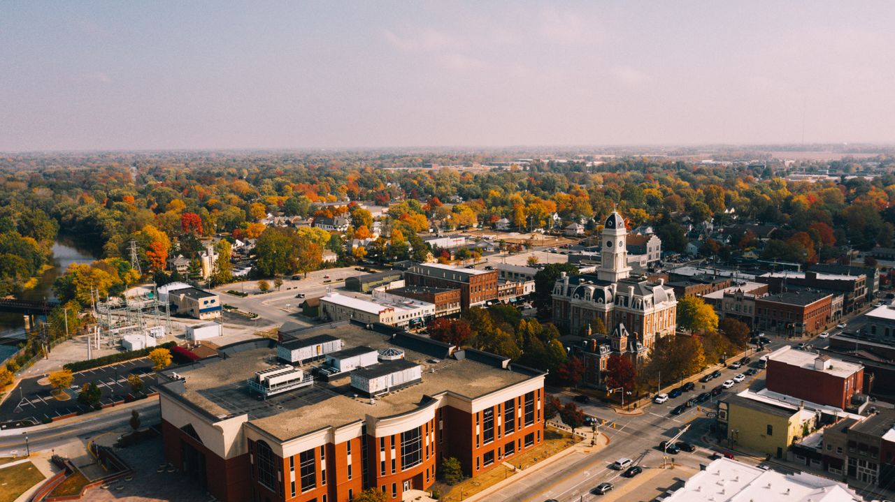 From above of aged building exteriors near roads and river behind bright trees in town in fall
