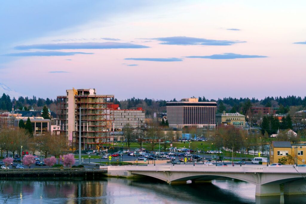 Vibrant cityscape featuring a bridge, buildings, and park under a pastel sky at dusk.