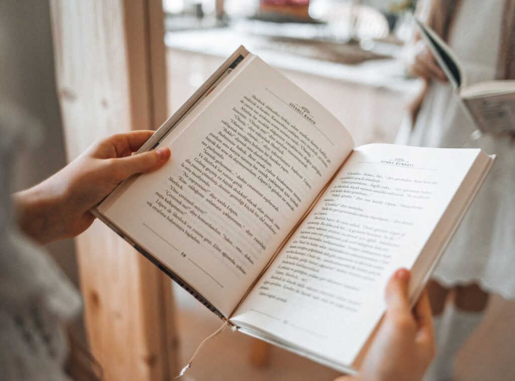 Close-up of hands holding an open book with blurred background indoors.